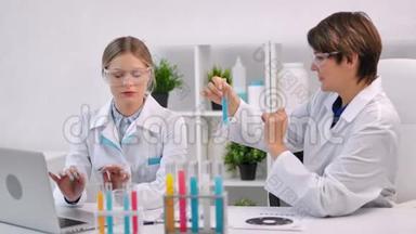 两位女医学家使用笔记本电脑在试管中使用彩色液体物质